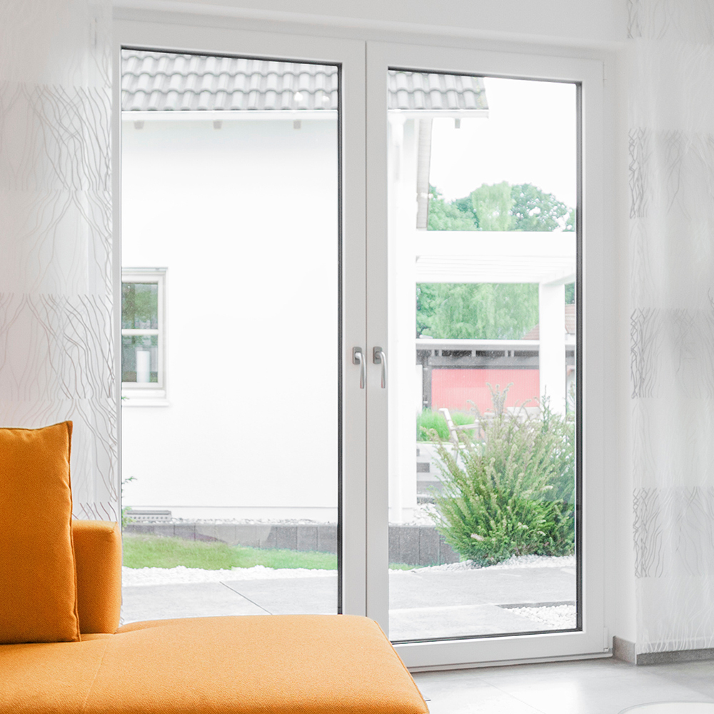 Eine weiße zweiflügelige Balkontür mit Blick vom Wohnraum aus nach Draußen